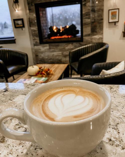 A cozy café scene featuring a latte with heart art, a fireplace, and comfortable seating in the background.