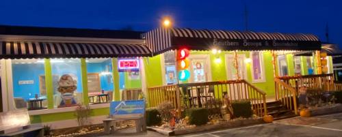 Brightly lit ice cream shop with a green exterior, striped awning, and an "Open" sign at dusk.