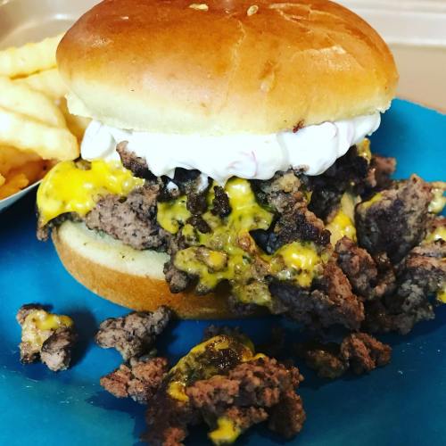 A messy cheeseburger with melted cheese and ground beef, served on a blue plate alongside a portion of fries.