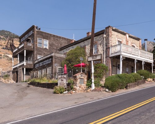 Historic building with wooden and stone architecture, featuring a porch, signage, and surrounding greenery on a sunny day.