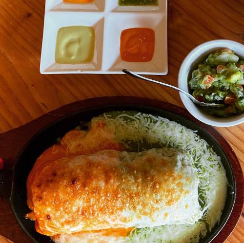 A sizzling burrito topped with melted cheese, served with guacamole and four dipping sauces on the side.