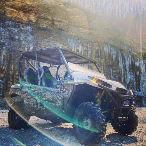 A muddy ATV parked near a rocky cliff with icicles, illuminated by sunlight.