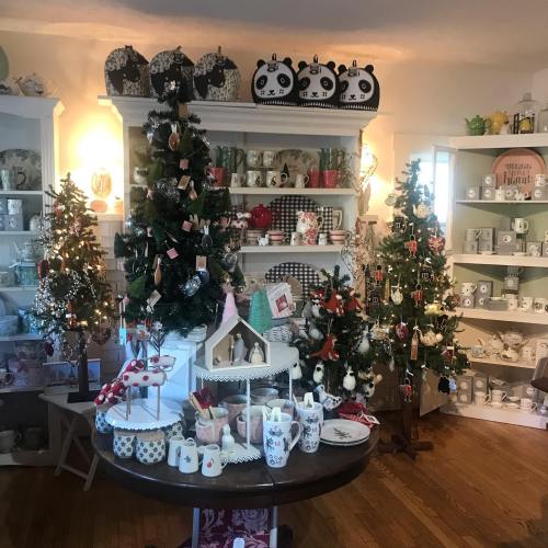 A cozy shop display featuring decorated Christmas trees, festive decor, and various holiday-themed items on shelves.