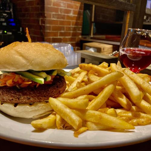 A plate featuring a burger with toppings and a side of golden fries, accompanied by a glass of red beverage.