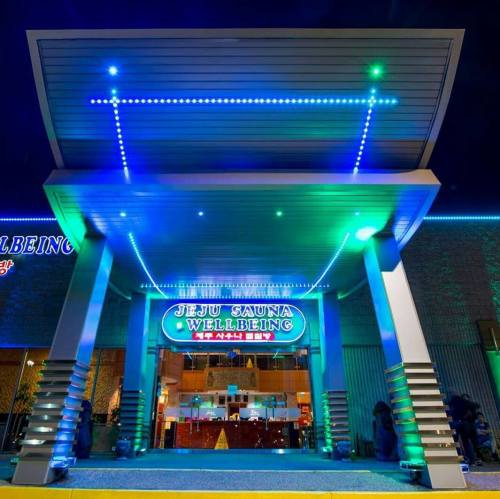 Brightly lit entrance of Jeju Sauna Wellbeing, featuring modern architecture and colorful LED lights at night.