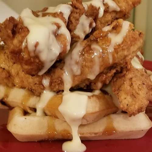 A stack of waffles topped with crispy fried chicken and drizzled with creamy sauce.