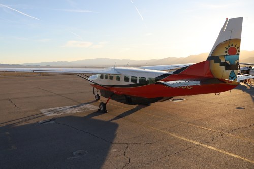 A colorful small aircraft parked on an airport tarmac with mountains in the background during sunset.