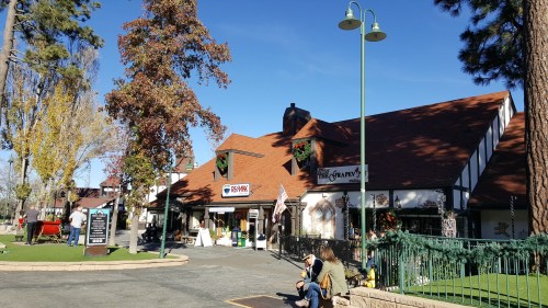 A quaint building with a red roof, surrounded by trees and festive decorations, in a sunny outdoor setting.