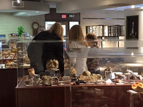 Three people examine rock and mineral displays in a museum exhibit, surrounded by various geological specimens.