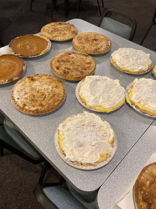 A table with various pies, including pumpkin and cream pies, arranged on a gray surface.