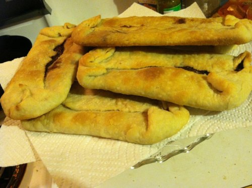 A stack of freshly baked pastries with a golden-brown crust, resting on a paper towel.