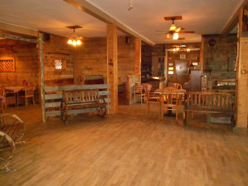 Cozy rustic interior of a wooden restaurant with benches and tables, featuring warm lighting and wooden walls.
