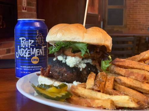 A juicy burger with bacon, lettuce, and blue cheese, served with fries and a can of Pour Judgement IPA.