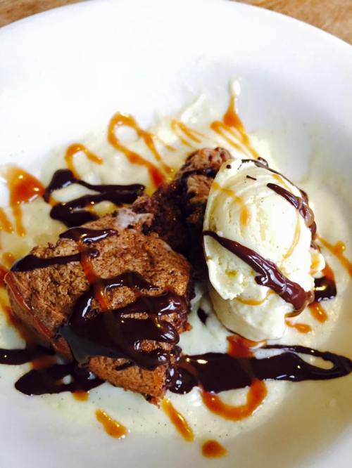 A dessert plate featuring warm chocolate cake, vanilla ice cream, and drizzles of caramel sauce.