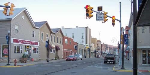 A quiet street scene with shops, traffic lights, and parked cars in a small town during early evening.