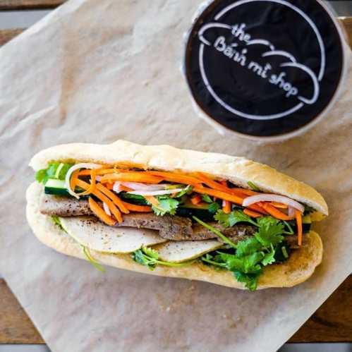 A fresh banh mi sandwich filled with vegetables, herbs, and meat, alongside a drink in a cup.