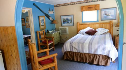 Cozy bedroom with a wooden bed, chair, and rustic decor, featuring blue walls and framed nature artwork.