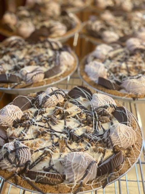 Close-up of decadent chocolate desserts topped with swirls of frosting, nuts, and drizzled chocolate on a cooling rack.