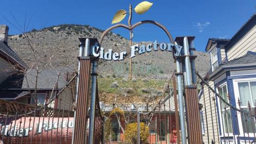 Sign for "Cider Factory" with a stylized apple, set against a mountainous backdrop and clear blue sky.