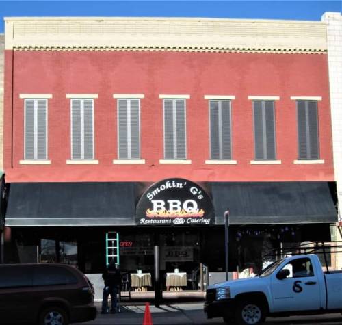 Exterior of Smokin' G's BBQ restaurant, featuring a red brick facade and a black awning with "OPEN" sign.