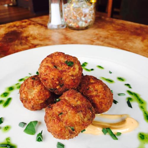 A plate with four golden-brown fried balls, garnished with green sauce and a dollop of creamy sauce on the side.