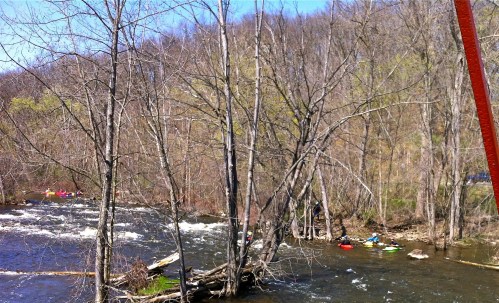 A scenic river with kayakers navigating the water, surrounded by trees and a hilly landscape in the background.