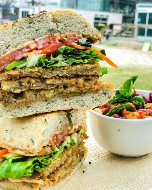 A stacked sandwich with crispy layers, lettuce, tomato, and carrots, served with a side of colorful salad.