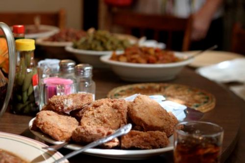 A table set with various dishes, featuring a plate of crispy fried chicken in the foreground and other sides in the background.