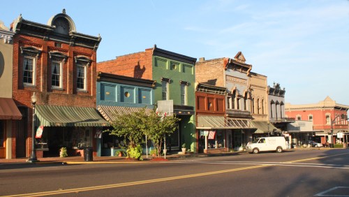 Historic buildings line a street, showcasing colorful facades and awnings under a clear blue sky.