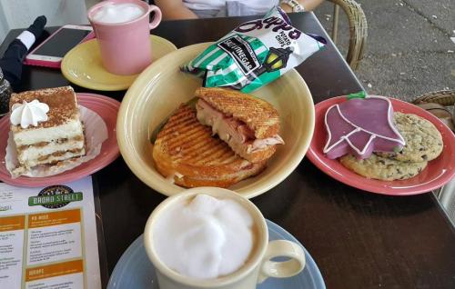 A table with a cappuccino, a sandwich, a cookie, and a slice of cake on colorful plates.