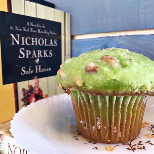 A green cupcake with nuts sits on a white plate next to a book titled "Safe Haven" by Nicholas Sparks.