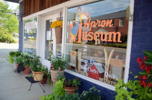 A storefront of the Apron Museum featuring colorful signage and potted plants along the sidewalk.