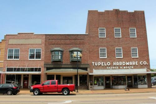 Historic brick buildings with storefronts, including Tupelo Hardware Co., and a red pickup truck parked in front.