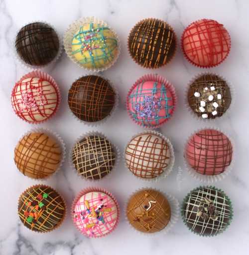 A variety of colorful, decorated cupcakes arranged in a grid on a marble surface.