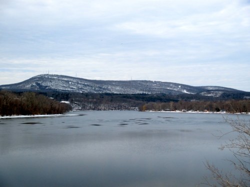 A serene river scene with snow-covered hills in the background under a cloudy sky.