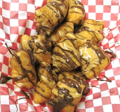 A basket of fried dough bites drizzled with chocolate and peanut butter sauce on a red and white checkered paper.