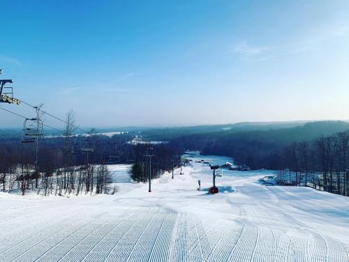 A snowy ski resort with groomed slopes, ski lifts, and a clear blue sky in the background.