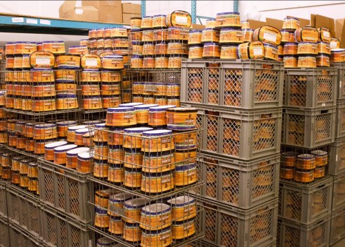 Stacks of orange and blue cans neatly arranged in gray crates within a warehouse setting.