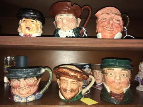 A collection of whimsical ceramic mugs with exaggerated facial features, displayed on a wooden shelf.