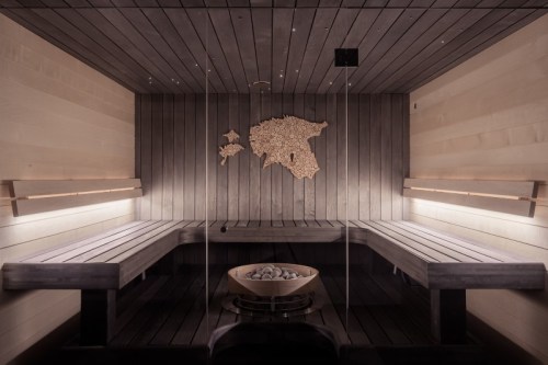 A modern sauna interior with wooden benches, a stone heater, and a map of a region on the wall. Soft lighting enhances the ambiance.
