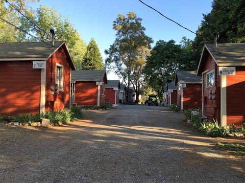 A gravel path lined with red cabins under a clear blue sky, surrounded by trees and greenery.