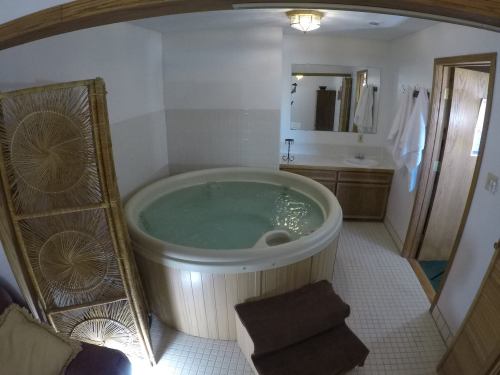 A spacious bathroom featuring a round hot tub, wooden accents, and a mirror above a sink. Soft lighting enhances the ambiance.