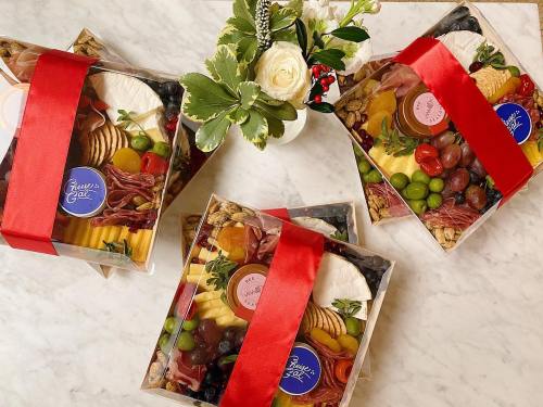 Three beautifully arranged charcuterie boxes with red ribbons, surrounded by fresh flowers on a marble surface.