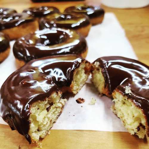 A close-up of chocolate-glazed donuts, one cut in half to reveal a fluffy interior, on a parchment-lined surface.
