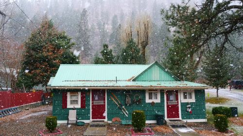 A green cabin with a metal roof in a snowy landscape, surrounded by trees and falling snowflakes.