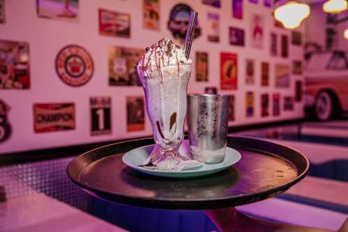 A delicious milkshake topped with whipped cream and chocolate drizzle, served on a tray in a retro-themed diner.