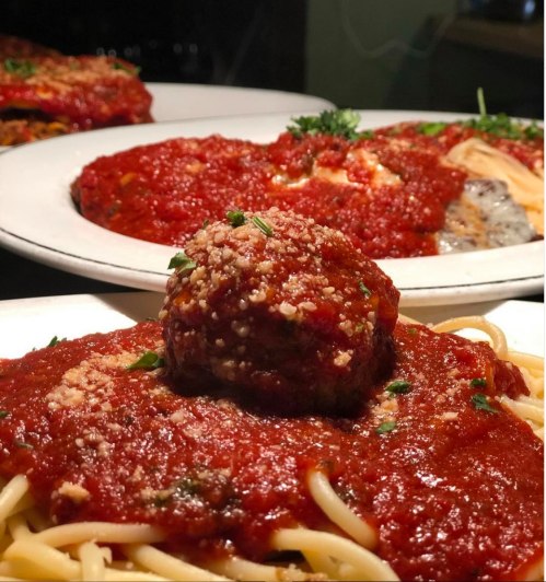 A plate of spaghetti topped with marinara sauce and a meatball, garnished with parsley and grated cheese.
