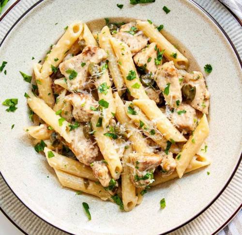 Creamy pasta dish with penne, chicken, capers, and fresh parsley, topped with grated cheese in a bowl.