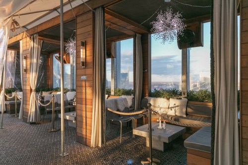 Cozy indoor lounge with wooden decor, large windows, and soft seating, featuring elegant lighting and a scenic view.