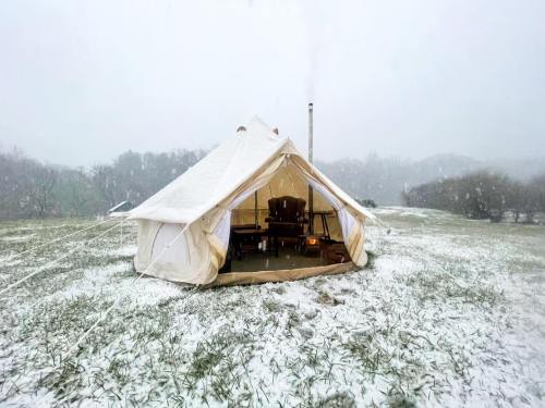 A cozy tent in a snowy landscape, with a wooden chair inside and snowflakes falling around.
